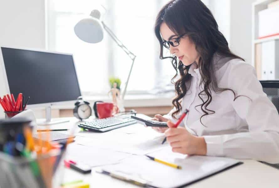 A female executive assistant works at a desk using a calculator and a pen