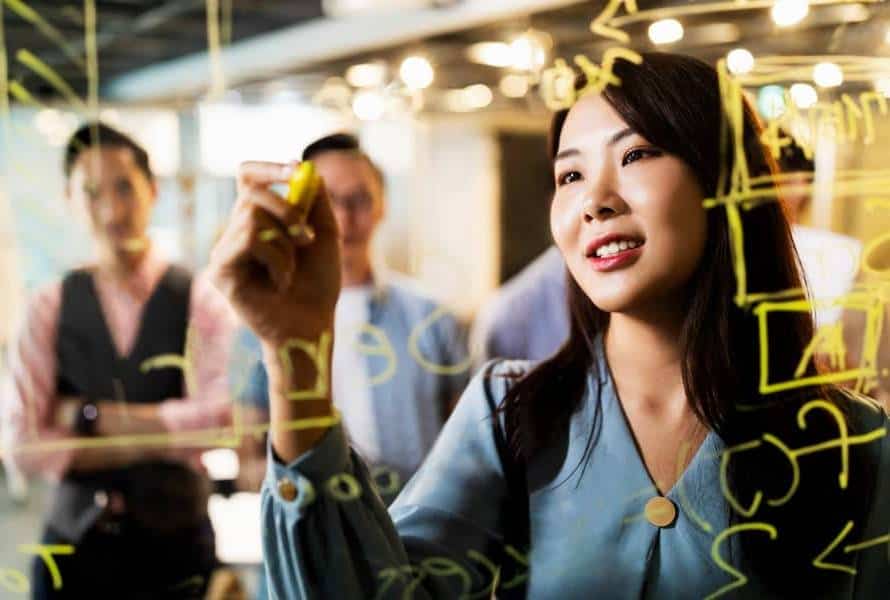 A woman writing out a project management plan on a glass wall for coworkers